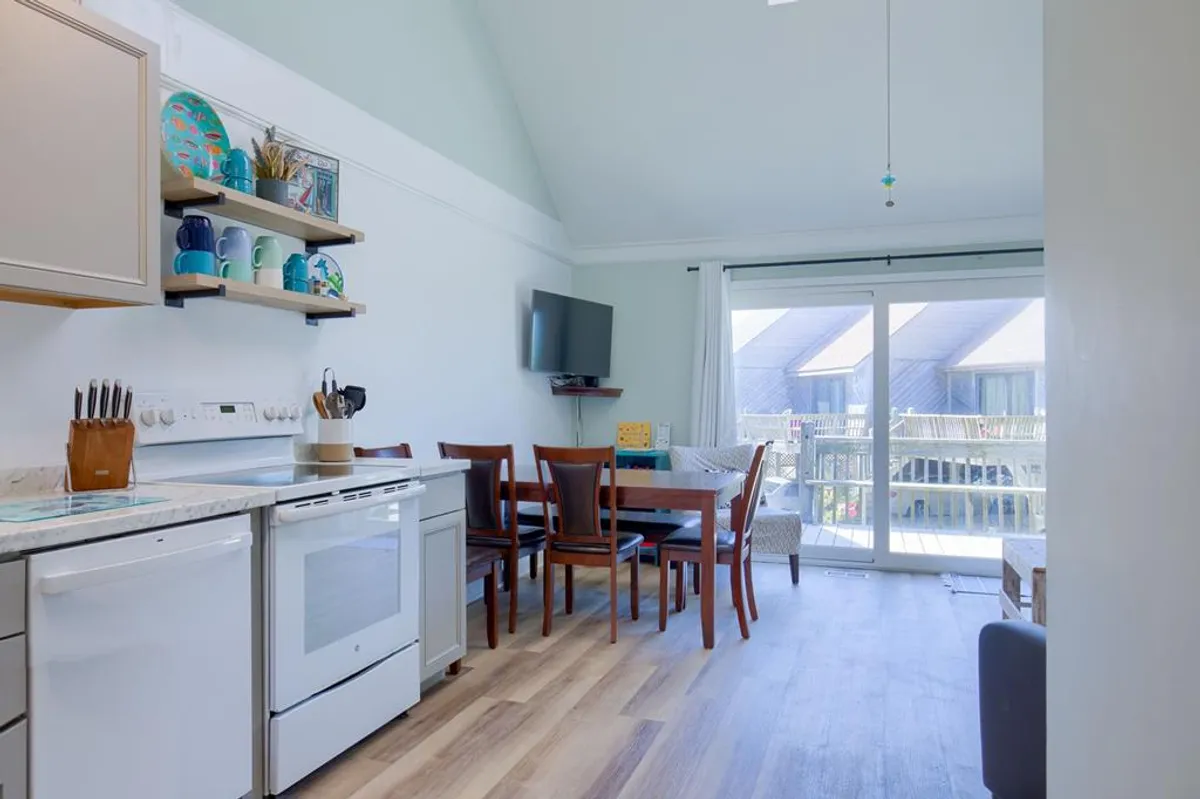 The kitchen and dining area is shown with modern appliances, a sunlit dining table, and large windows. The setting is inviting for families or groups to enjoy shared meals or casual gatherings in a bright, cheerful space.