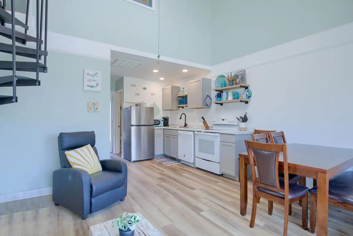 A bright and modern living area showcasing a unique spiral staircase leading up to a playful loft. The space features gray kitchen cabinets, a dining table for shared meals, and a reclining chair for relaxation.