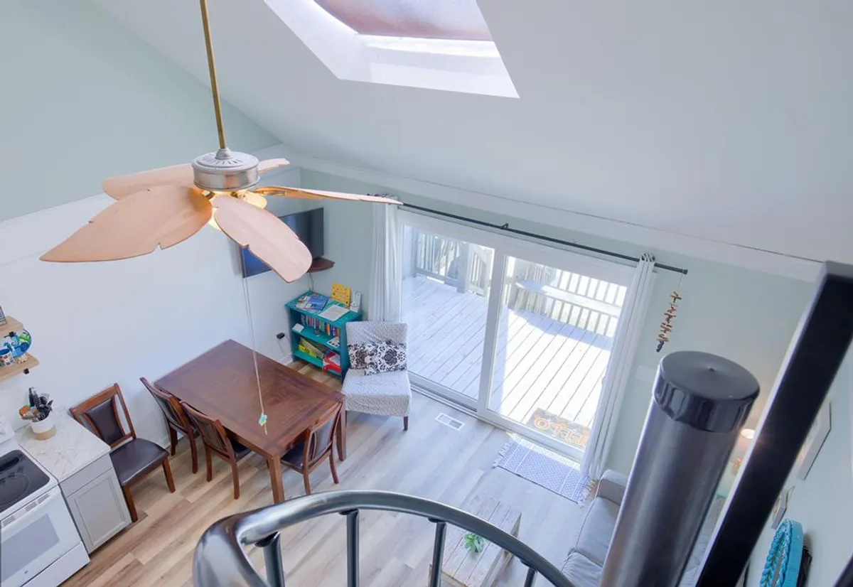 A cozy dining area with a table, ceiling fan, large windows letting in natural light, and an adjacent sitting area. The space feels comfortable and ideal for gathering for meals or games, with views that connect the indoors to the outside.