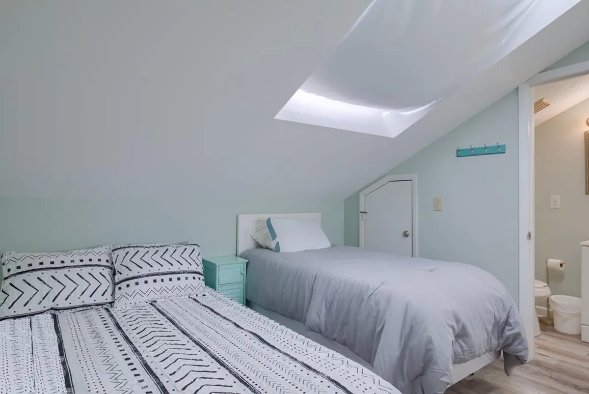A serene bedroom scene with a cozy bed featuring patterned bedding, light blue accent furniture, and a skylight that floods the room with natural light. The overall ambiance is calm and soothing, perfect for relaxation or restful sleep.