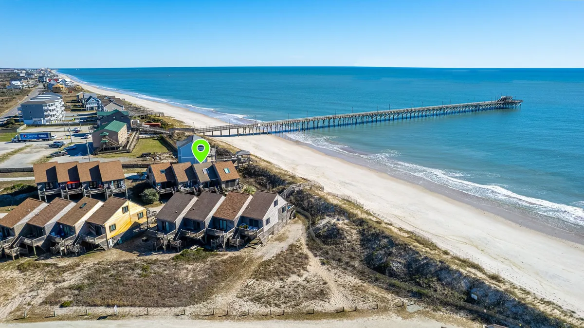 This image shows a stunning exterior view of beachfront properties set against the ocean, with a pier stretching out over the water. The beach is wide and inviting, and the pier—a focal point in the distance—clearly suggests opportunities for fishing and seaside strolls. The mood is relaxed and sunny, perfectly capturing the vibrant spirit of coastal exploration and leisurely activities.