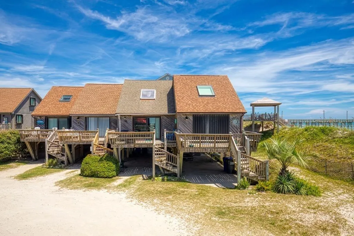 A spacious wooden deck surrounded by palm trees, offering lounging areas with views of the nearby beach. The deck is well-suited for outdoor gatherings and features a skylight overhead, blending natural light with a welcoming, relaxed ambiance.