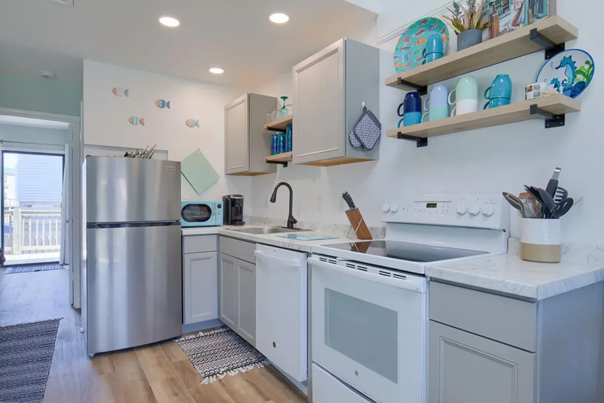 This cheerful kitchen scene highlights stainless steel appliances, colorful dishware on open shelves, a modern sink, and playful decorative fish wall art. The space is bright and well-appointed, suggesting a welcoming environment for cooking and social gatherings.