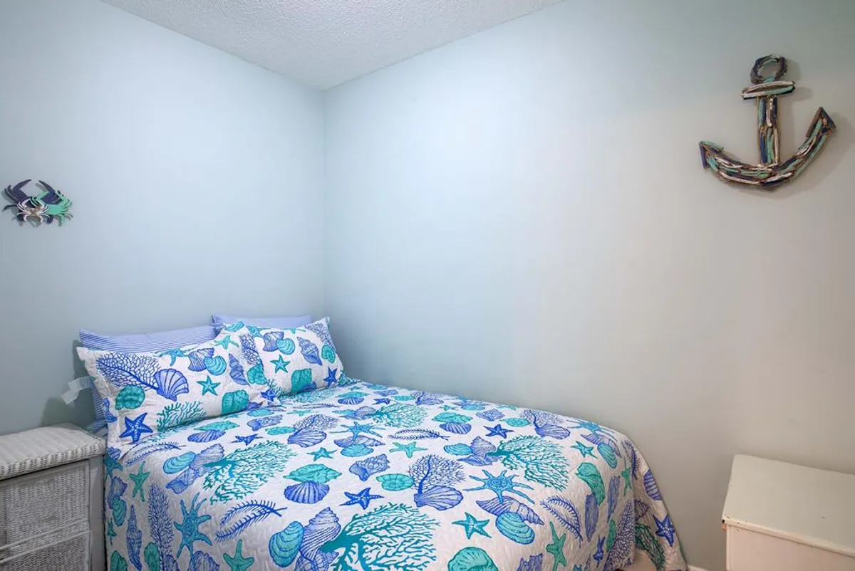A serene guest bedroom with ocean-themed bedding, colorful fish and anchor wall decor, and a calm, light-filled atmosphere—inviting guests to unwind after a day by the sea.