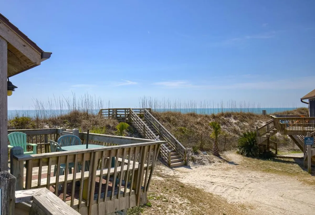 This image captures a beachfront deck with steps leading directly to the sandy beach. The view includes tropical plants, the ocean, and inviting steps, highlighting the seamless connection between the property and the sand.
