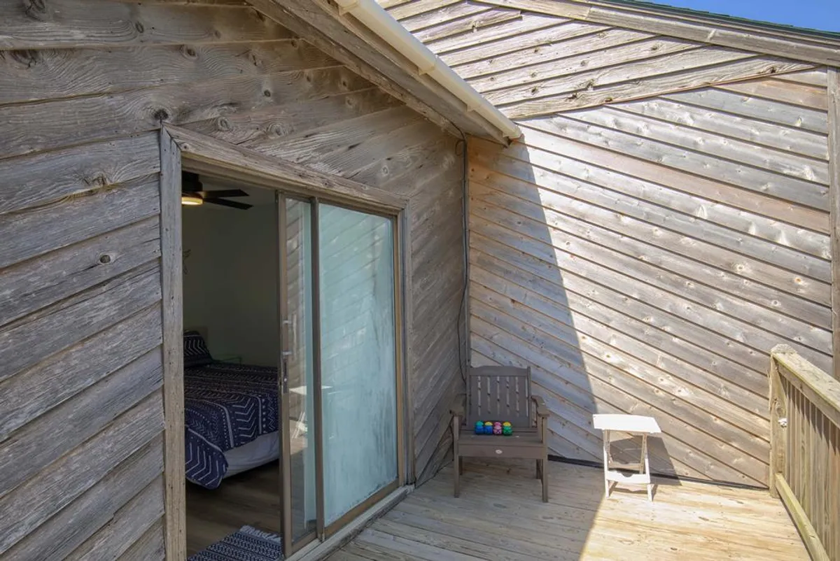 An exterior view of a wooden deck accessed via a glass sliding door, with comfortable seating and a tranquil setting. The arrangement suggests a seamless flow from the interior living area to the outdoors, perfect for enjoying morning coffee, sunsets, or evening gatherings under the stars.